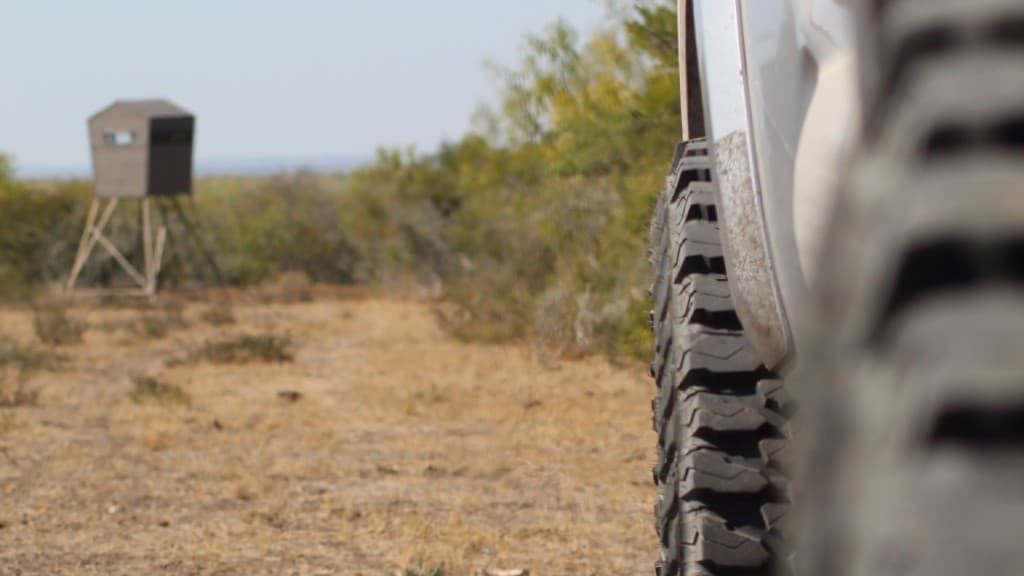 Close-up of off-road tires on a ranch road with a hunting blind in the blurred background